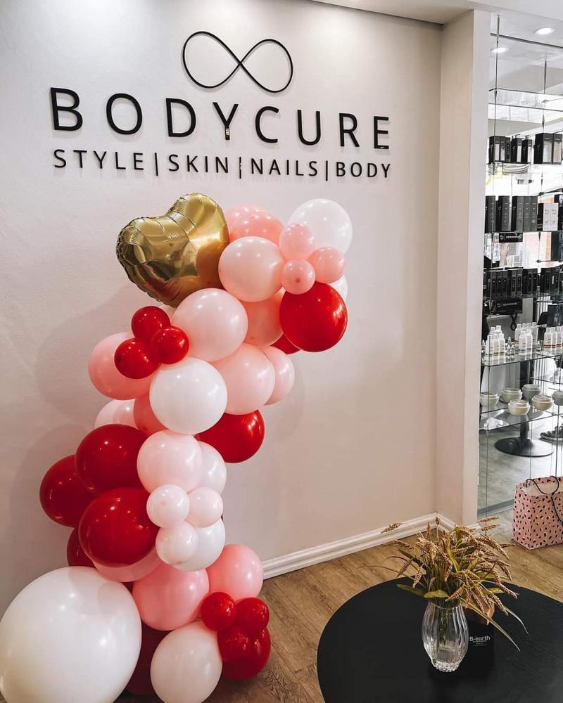 Red, pink and white organic balloon garland with a gold heart balloon beside the signage wall of a beauty and nails salon