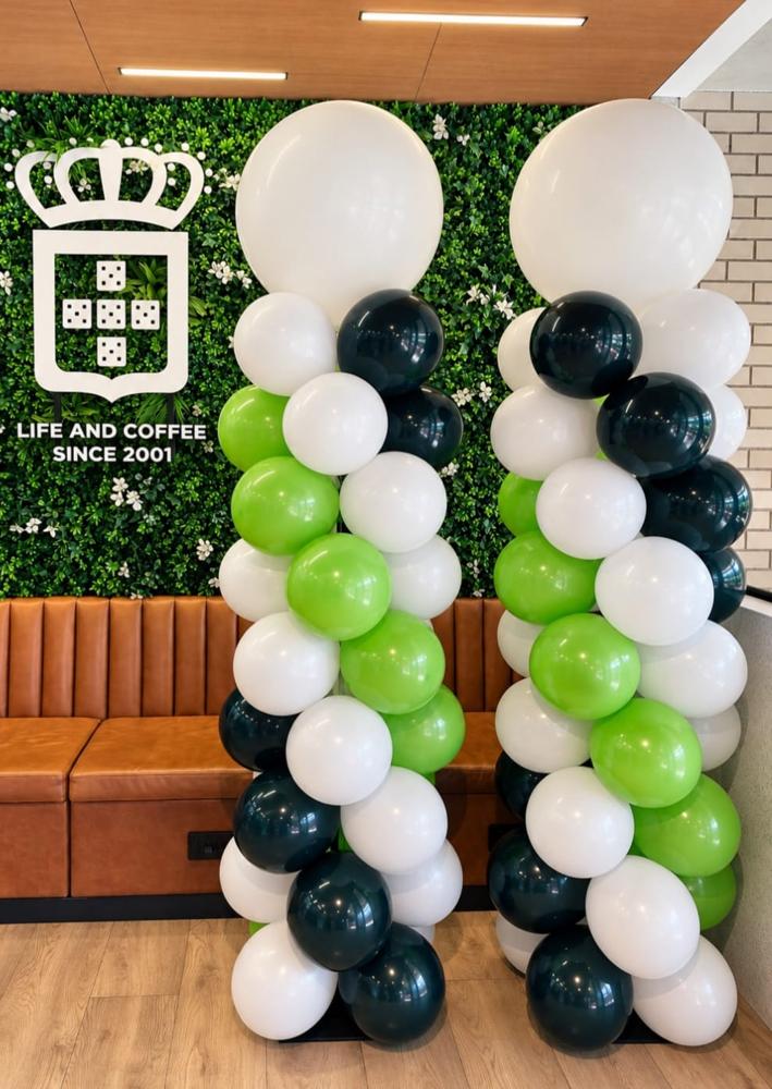 Twin white, lime and dark green balloon columns flanking a branded living-wall logo inside a coffee franchise store