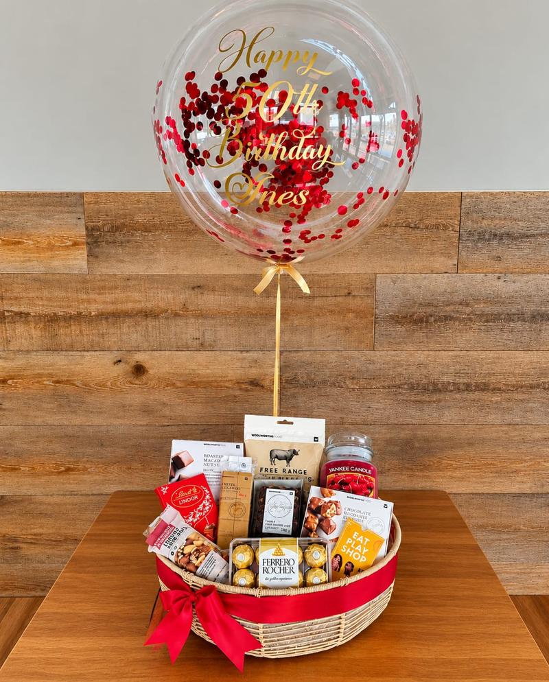 Red confetti bubble balloon with gold 50th birthday lettering above a wicker hamper of gourmet treats, chocolates and a scented candle
