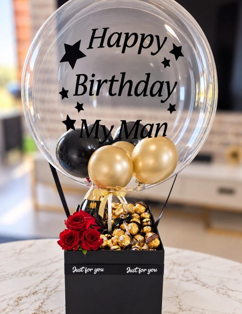 Black and gold printed bubble balloon above a black gift box filled with Ferrero Rocher chocolates and red roses