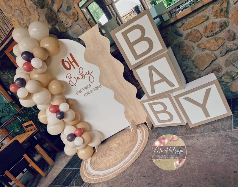 Oh Baby shower backdrop with nude, cream and terracotta balloon garland, a wavy timber panel and BABY letter blocks