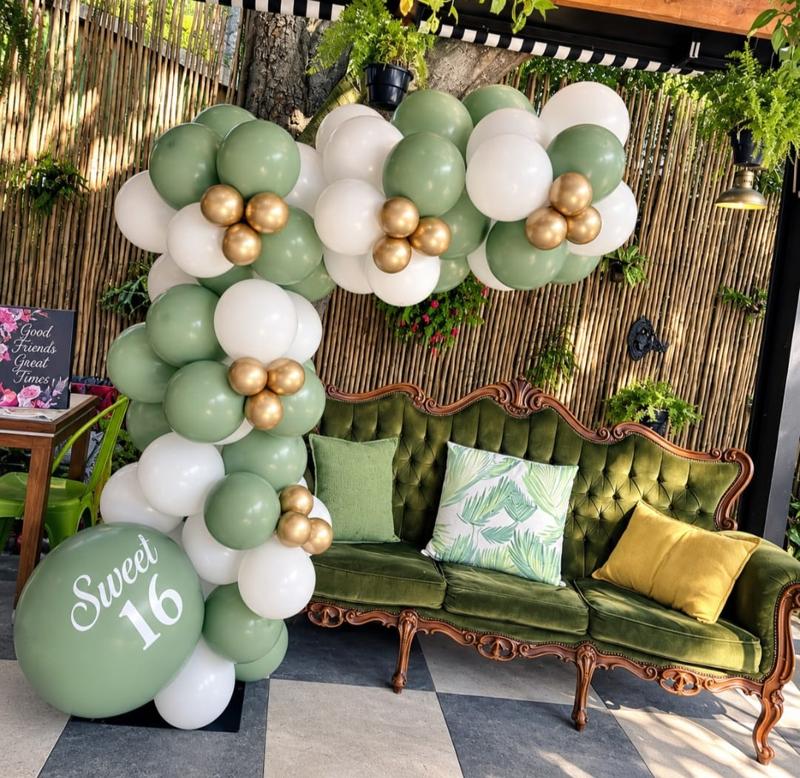 Sage green, white and chrome gold organic balloon garland above a green velvet couch with a printed Sweet 16 jumbo balloon