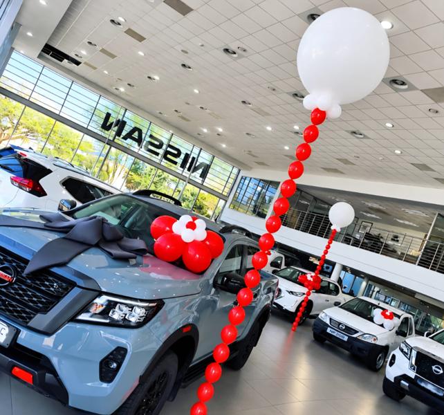 Red balloon chains, white jumbo ceiling toppers and a large ribboned bow dressing new vehicles across a national motor dealership showroom floor