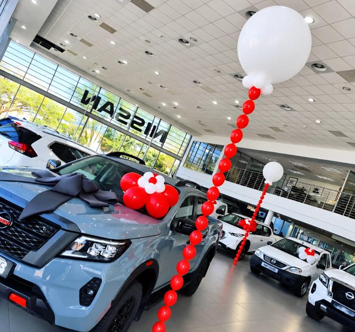 Red balloon chains, white jumbo toppers and a ribboned bow dressing new vehicles on a motor dealership showroom floor