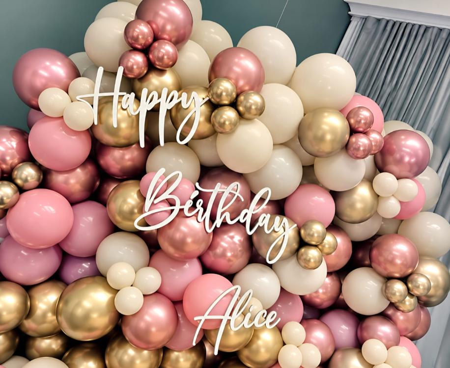 Organic balloon garland backdrop in rose, cream and chrome gold behind personalised script signage