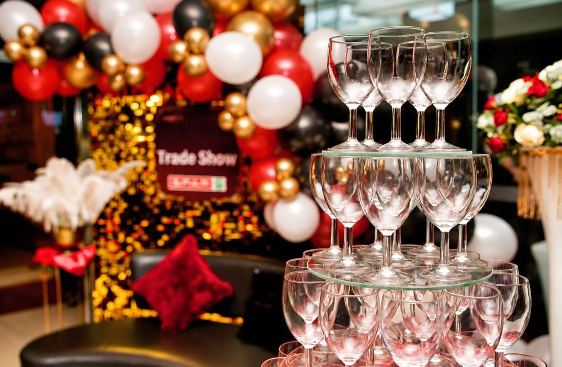 Corporate trade show stand styled with a balloon garland, sequin backdrop and champagne tower